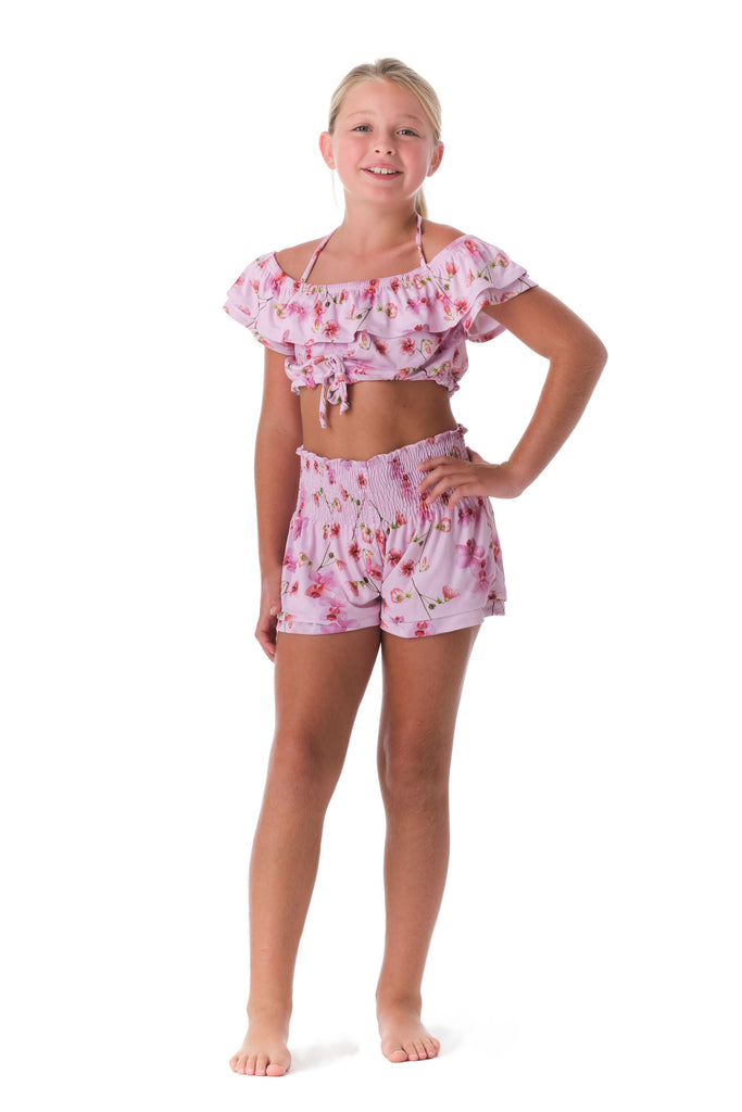 Girl is wearing Submarine Designer Swimwear Top Notch orchids pink print off-the-shoulder ruffled top.